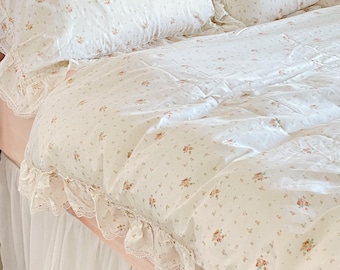 May include: White bedding with a delicate floral pattern and lace trim. The bedding is arranged on a bed with a white ruffled bed skirt.