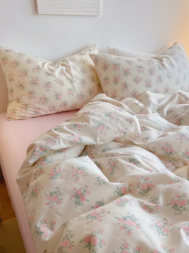 Puede incluir: Un juego de cama blanco con un estampado floral rosa. El juego incluye una funda n&oacute;rdica, dos fundas de almohada y una s&aacute;bana bajera.