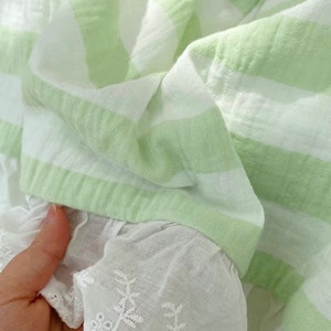 May include: A green and white striped fabric with a white lace trim. The fabric is soft and has a textured look.