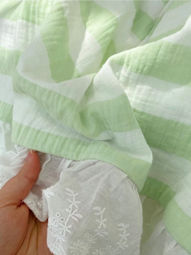 May include: A green and white striped fabric with a white lace trim. The fabric is soft and has a textured look.