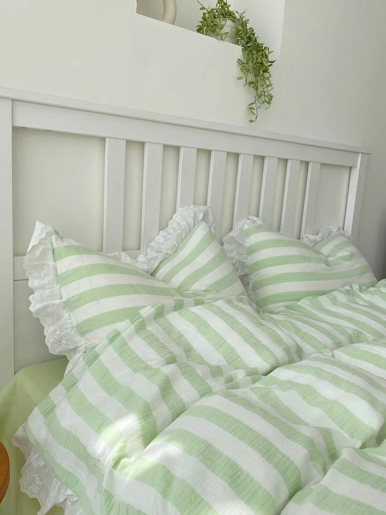 May include: Green and white striped bedding with white lace trim. The bedding is on a white bed frame with a white headboard.