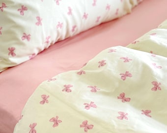 May include: White bedding with a pink bow pattern. The bedding is made of soft, comfortable fabric and features a subtle pink bow design.