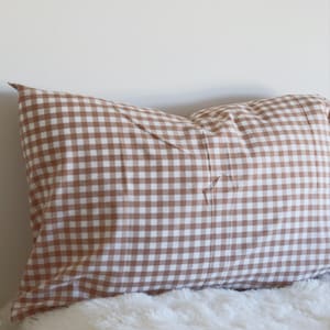 May include: A brown and white gingham patterned pillow. The pillow is rectangular and rests on a white, fluffy surface. The pillow is a warm, neutral color and would complement a variety of decor styles. The image includes the text "Pegycrafts" and "ALL RIGHTS RESERVED".