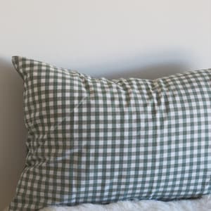 May include: A rectangular pillow with a green and white gingham pattern. The pillow is resting on a white, fluffy surface. The pillow is against a white wall. The text "&copy;Pegycrafts ALL RIGHTS RESERVED" is visible.