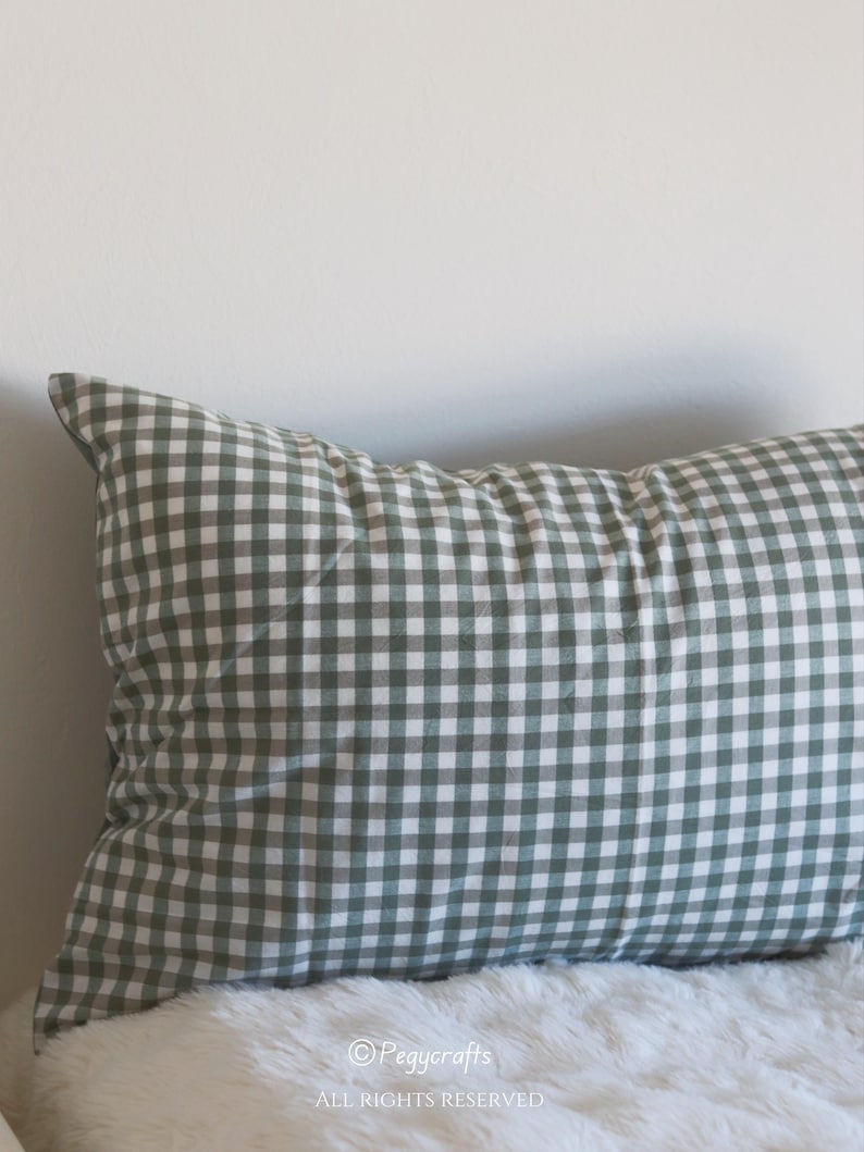 May include: A rectangular pillow with a green and white gingham pattern. The pillow is resting on a white, fluffy surface. The pillow is against a white wall. The text "&copy;Pegycrafts ALL RIGHTS RESERVED" is visible.