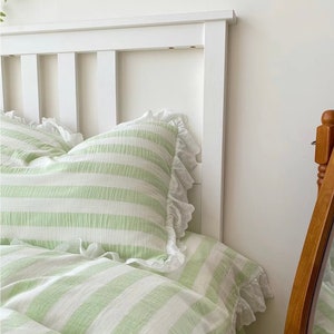 May include: A white bed frame with a green and white striped duvet cover and pillowcases. The duvet cover and pillowcases have white lace trim.