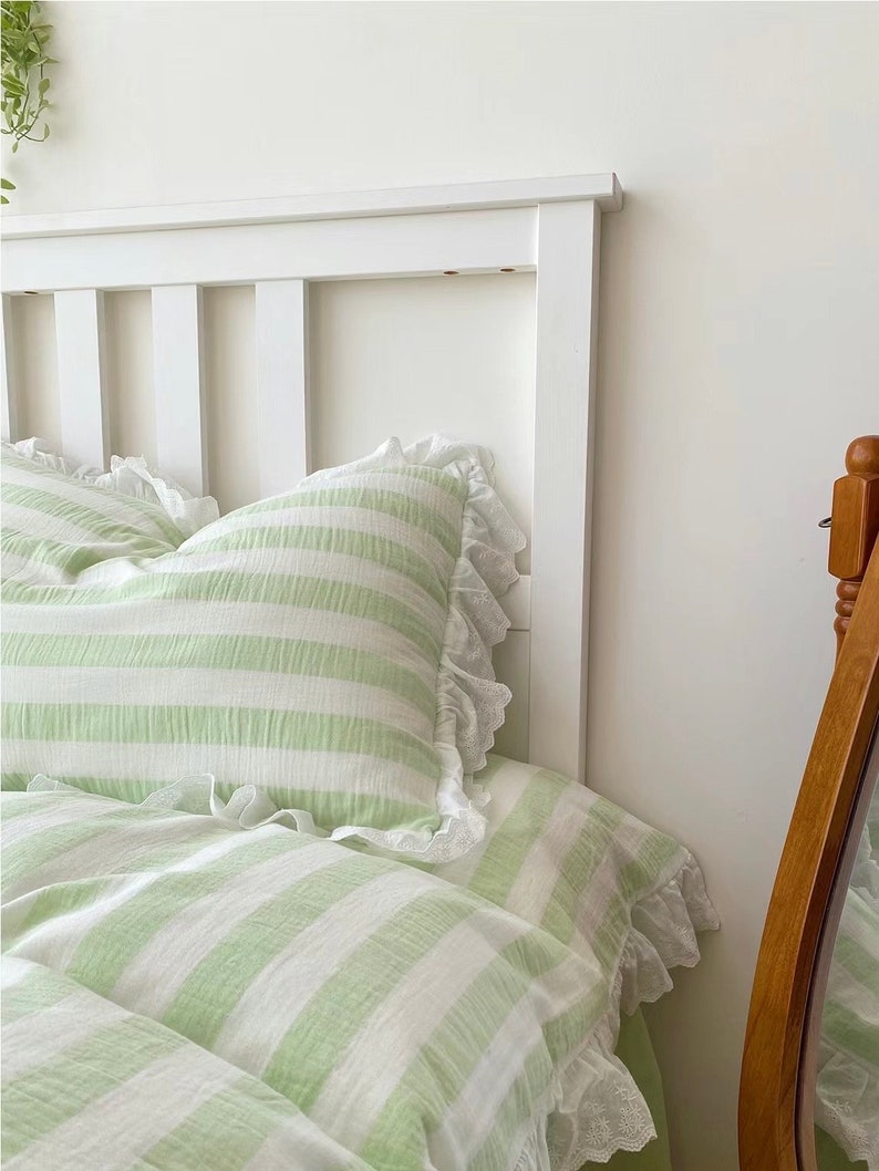 May include: A white bed frame with a green and white striped duvet cover and pillowcases. The duvet cover and pillowcases have white lace trim.