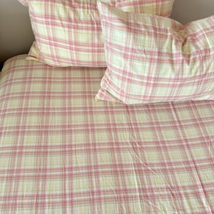 Puede incluir: Un juego de cama con un diseño de cuadros amarillos y rosas. El juego incluye dos almohadas y una funda nórdica. La tela tiene un aspecto suave y texturizado. La estética general es clásica y campestre.