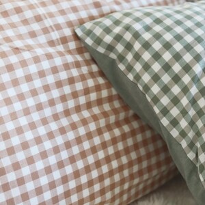 May include: Close-up of two decorative pillows with a gingham pattern. One pillow features a brown and white checkered design, while the other has a green and white checkered pattern. The pillows are soft and inviting, perfect for home decor.