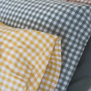 May include: Close-up of three rolls of fabric in yellow, green, and brown gingham patterns. The yellow fabric is in the foreground, followed by green and then brown. The fabric is folded and layered, showing the texture and color variations.