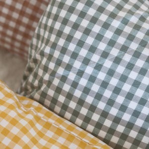 May include: Close-up of three gingham-patterned pillows in shades of brown, green, and yellow. The pillows are soft and textured, with a classic checkered design. The image includes the text "&copy; Pegycrafts ALL RIGHTS RESERVED".