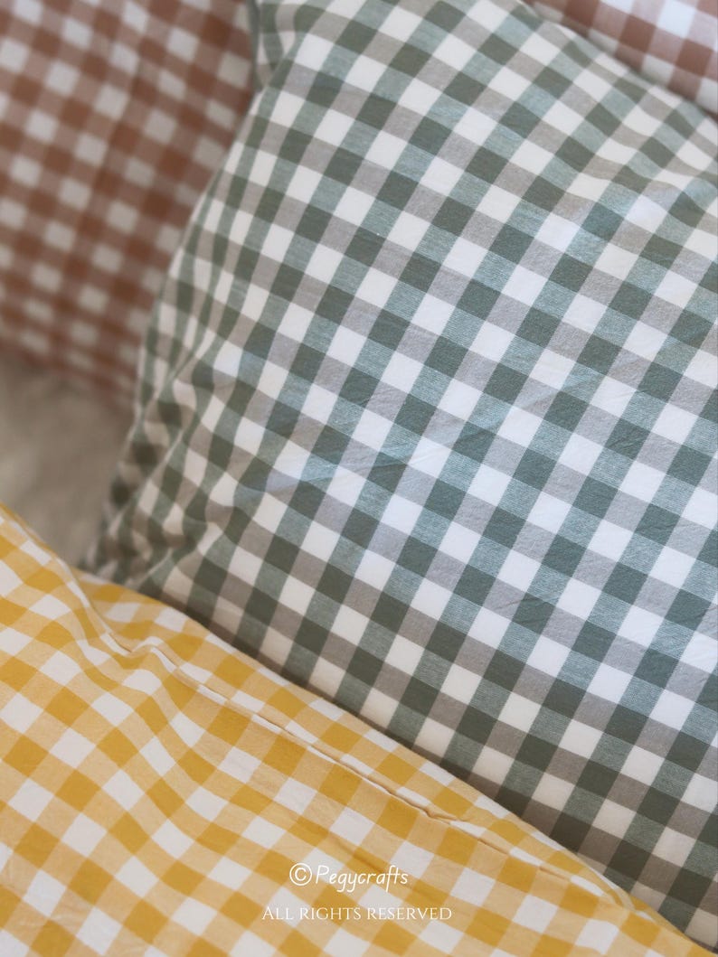 May include: Close-up of three gingham-patterned pillows in shades of brown, green, and yellow. The pillows are soft and textured, with a classic checkered design. The image includes the text "&copy; Pegycrafts ALL RIGHTS RESERVED".