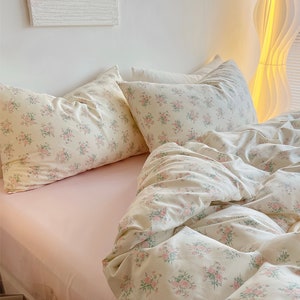 Puede incluir: Una cama rosa con un edred&oacute;n de estampado floral blanco y dos fundas de almohada a juego. La cama est&aacute; hecha con una s&aacute;bana blanca y una manta rosa.
