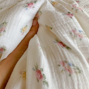 May include: White cotton fabric with a floral pattern of small pink, yellow, and blue flowers. The fabric is soft and textured, and it is perfect for making clothing, bedding, or other home decor items.