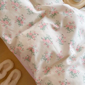 Puede incluir: Un juego de cama blanco con un delicado estampado floral con rosas rosas y hojas verdes. La ropa de cama est&aacute; hecha de tela suave y c&oacute;moda y es perfecta para agregar un toque de elegancia a cualquier dormitorio.