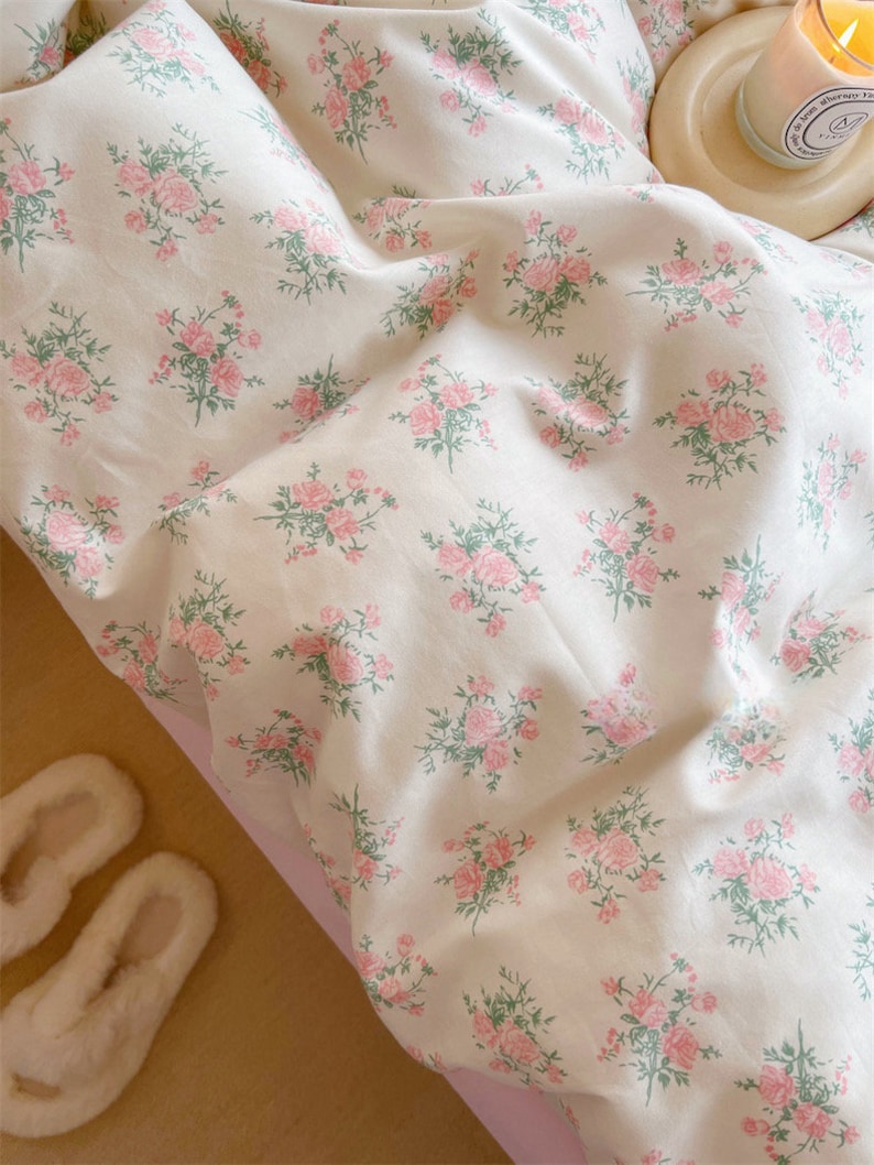 Puede incluir: Un juego de cama blanco con un delicado estampado floral con rosas rosas y hojas verdes. La ropa de cama est&aacute; hecha de tela suave y c&oacute;moda y es perfecta para agregar un toque de elegancia a cualquier dormitorio.
