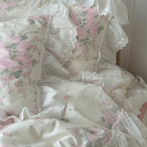 May include: A white bed with a floral patterned duvet cover and pillowcases. The bedding features delicate lace trim and a pale pink floral pattern.