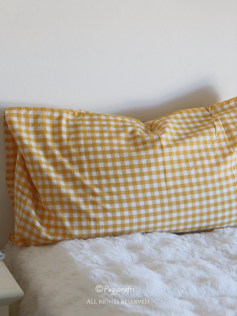 May include: A rectangular pillow with a yellow and white gingham pattern. The pillow is resting on a white, fluffy surface. The image includes the text "&copy; Pegycrafts ALL RIGHTS RESERVED".