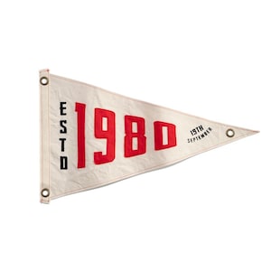 May include: Cream pennant flag with red text. The flag reads "ESTD 1980 19th September". The pennant has metal eyelets for hanging. The flag is triangular in shape.