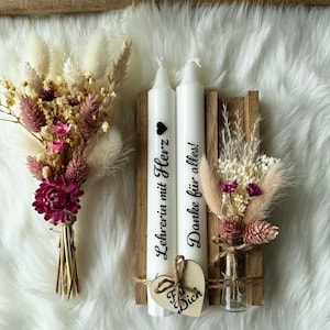 Könnte beinhalten: Zwei weiße Kerzen mit dem Text "Lehrerin mit Herz" und "Danke für alles!" darauf. Die Kerzen stehen in einem Holzhalter mit einer kleinen Vase mit Trockenblumen. Ein kleines Holzhäuschen mit dem Text "Für Dich" steht vor den Kerzen.