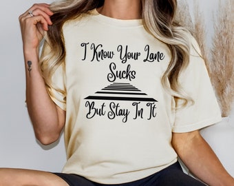 May include: A cream colored t-shirt with black text that reads "I Know Your Lane Sucks But Stay In It". The text is displayed over a black graphic of a set of stairs.