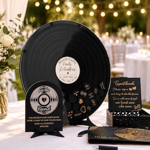 May include: A circular black vinyl record guestbook frame with a white center label reading Emily & Geoffrey 10.05.2026, accompanied by a small arched sign saying for the Record, a black wooden box for heart tokens, and a matching black guestbook.