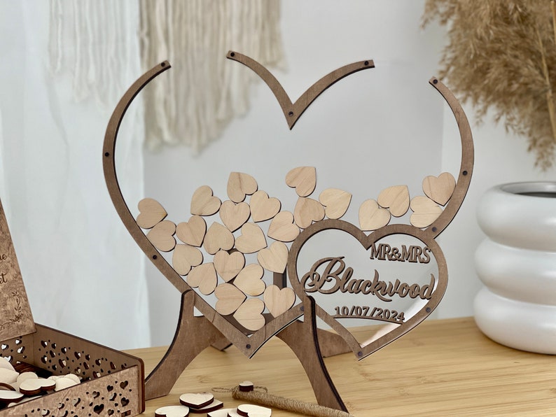 May include: Wooden heart-shaped wedding guest book with a clear acrylic insert. The hearts are decorated with the names "MR & MRS Blackwood" and the date "10/07/2024".