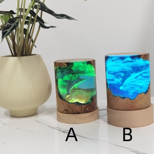 May include: Two resin lamps with a dolphin inside, one with a green and blue resin and the other with a blue resin. The lamps are on wooden bases labeled A and B.