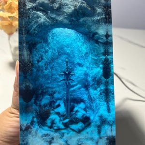 May include: A blue glass sculpture of a sword in a cave. The sword is silver and the cave is made of blue glass with white swirls.