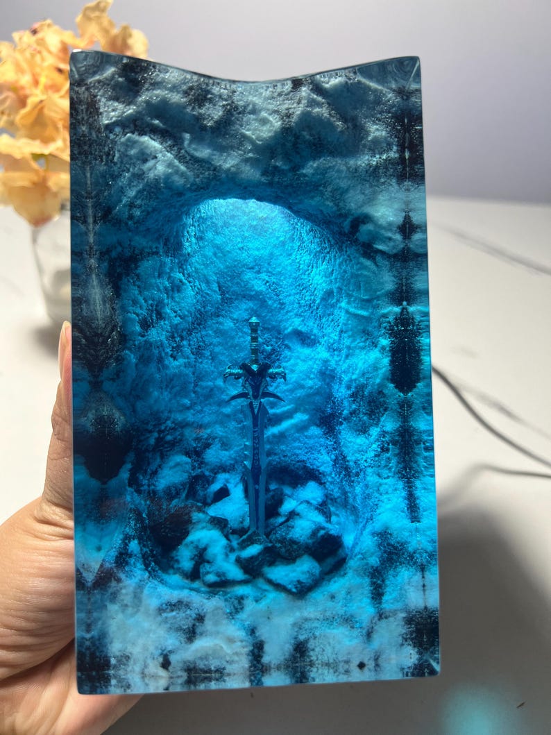 May include: A blue glass sculpture of a sword in a cave. The sword is silver and the cave is made of blue glass with white swirls.