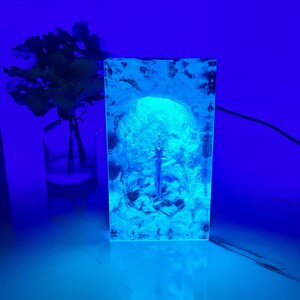 May include: A clear glass lamp with a blue light shining through it, creating a glowing effect. The lamp is shaped like a human head and has a textured surface.
