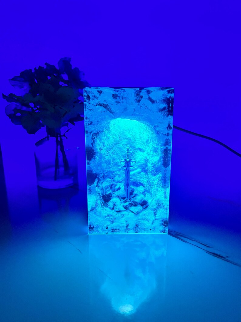 May include: A clear glass lamp with a blue light shining through it, creating a glowing effect. The lamp is shaped like a human head and has a textured surface.