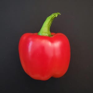 May include: A single red bell pepper with a green stem on a black background.