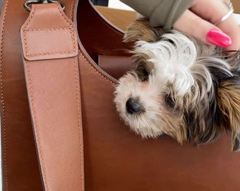 May include: A small, white and brown dog with black eyes peeks out of a brown leather tote bag.
