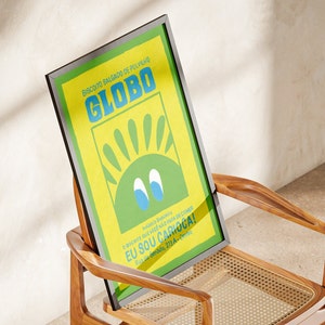 May include: A framed poster with a yellow background and a green sun with blue eyes. The poster says "Biscoito Salgado de Polvilho GLOBO" and "EU SOU CARIOCA!" in Portuguese.