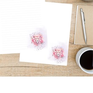 May include: White lined stationery and notecards with a watercolor lion design. The lion is surrounded by pink roses and text that reads "Strength and Honor". A pen, coffee cup, and plant are also visible.