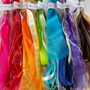 Puede incluir: Una colección de cintas multicolores dispuestas en un espectro, incluyendo rosa, rojo, naranja, amarillo, verde, azul, morado y beige. Cada cinta presenta una etiqueta blanca impresa con el texto twin paper birds en el borde superior.