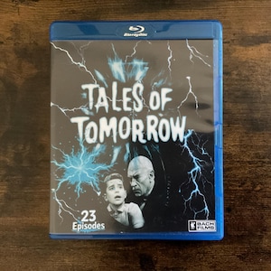 Peut inclure: Un boîtier Blu-ray bleu pour Tales of Tomorrow avec un fond noir et des éclairs blancs. La couverture présente une image en noir et blanc d'une jeune personne et d'une personne âgée, avec le texte 23 Episodes et le logo Bach Films.