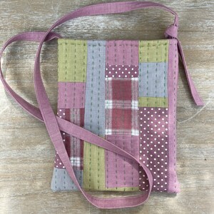 May include: A small pink and green patchwork fabric bag with a long strap. The bag features a variety of patterns including polka dots, plaid, and stripes.