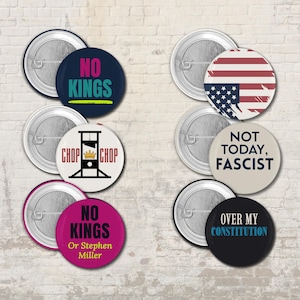 Puede incluir: Un conjunto de botones redondos con varios diseños y texto. Un botón presenta la bandera estadounidense. Otros botones tienen frases como "NO KINGS", "CHOP CHOP" y "NOT TODAY, FASCIST". Los botones son de varios colores.