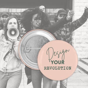 Könnte beinhalten: Ein hellrosa Knopf mit dem Text "Design Your Revolution" in dunkelgrüner Schrift. Der Knopf ist rund und hat eine Metallnadel auf der Rückseite. Der Hintergrund zeigt eine Gruppe von protestierenden Menschen.
