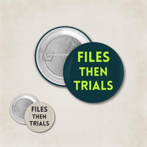 Könnte beinhalten: Drei runde Ansteckbuttons. Einer ist dunkelblaugrün mit den Worten "FILES THEN TRIALS" in leuchtendem Grün. Die anderen beiden sind silber und weiß mit dem gleichen Text in Schwarz.