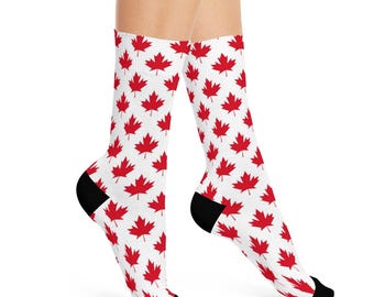 May include: White socks with a repeating pattern of red maple leaves. The socks have black heels and toes. The maple leaf design is a symbol of Canada.