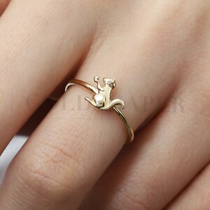 May include: A gold ring with a squirrel design. The squirrel is sitting on its hind legs with its tail curled up.