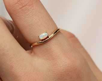 Puede incluir: Un delicado anillo de oro con una banda curva y una pequeña piedra de ópalo ovalada.