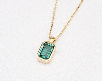 May include: A gold chain necklace with a green gemstone pendant. The pendant is a rectangular emerald cut.