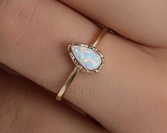 Puede incluir: Un delicado anillo de oro con una piedra de ópalo en forma de lágrima. El ópalo tiene una base blanca con destellos iridiscentes de color.