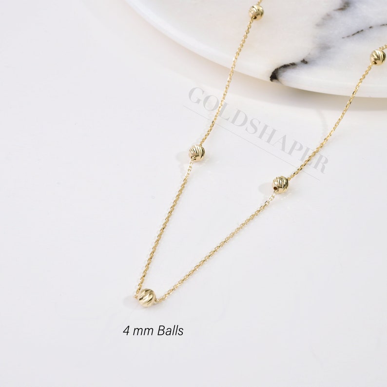 May include: A gold necklace with a delicate chain and five 4 mm round balls. The necklace is on a white background.