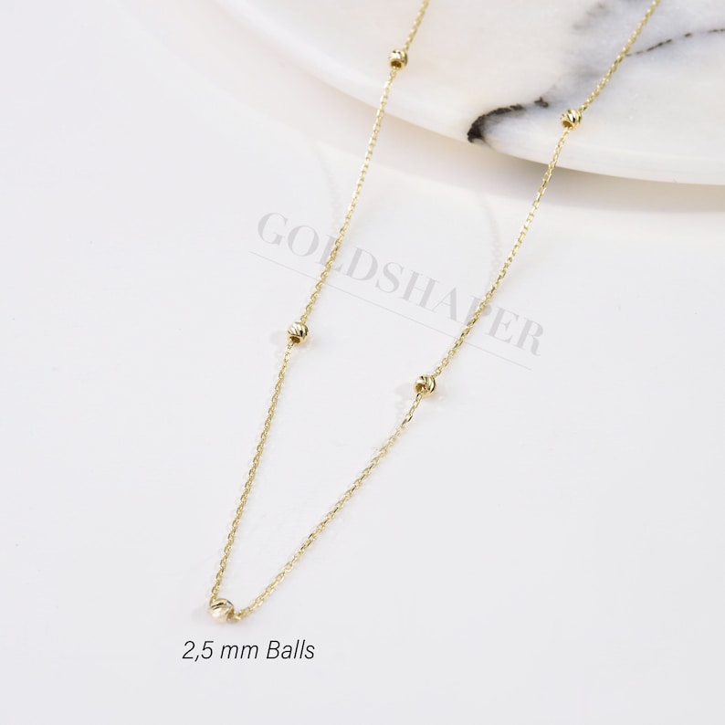 May include: A gold chain necklace with small, round balls. The balls are 2.5 mm in diameter. The chain is delicate and has a simple design.