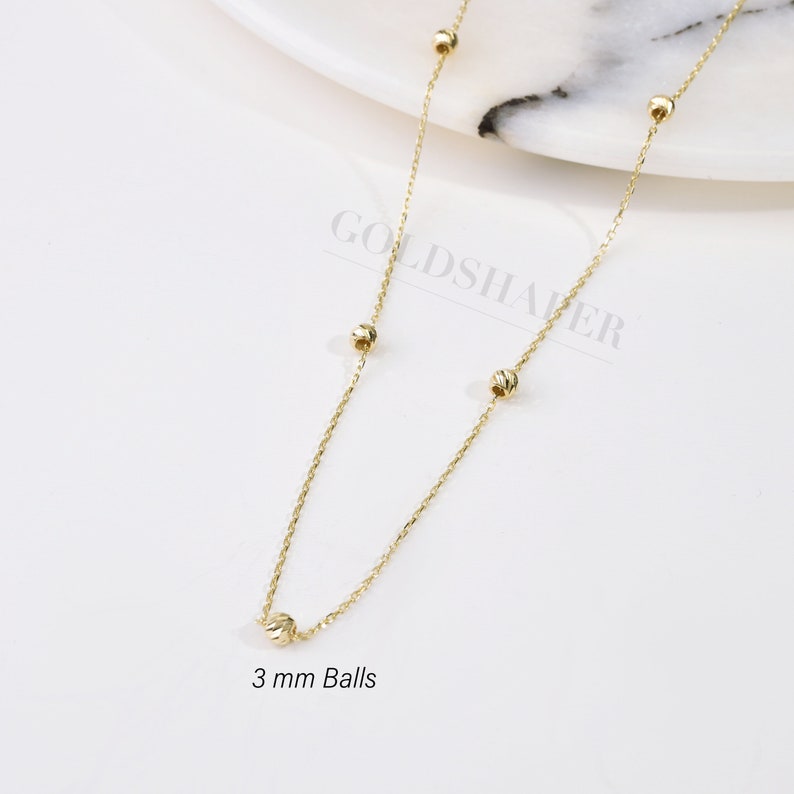 May include: A gold chain necklace with five 3 mm balls. The chain is delicate and has a simple design.